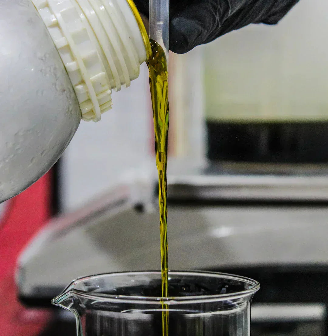 Pouring natural oil into a beaker in a laboratory setting.