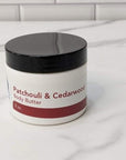 Patchouli & Cedarwood Body Butter jar on marble surface, offering luxurious hydration and warm, earthy aroma.