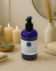 Blue bottle of Patchouli & Cedarwood liquid hand soap with pump dispenser on beige spa table with candles and towel