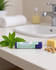 All-natural peppermint lip balm tube on bathroom counter with mint leaves, natural oils, and moisturizing ingredients nearby.