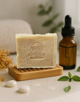 Sea Moss and Tea Tree natural bar soap on wooden soap dish with dropper bottle and green leaves, skincare setup
