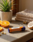 Sweet Orange Lip Balm tube on countertop with fresh orange slices and coconut halves, natural moisturizing lip care product