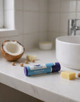Tube of unscented lip balm on bathroom countertop with coconut and shea butter ingredients nearby
