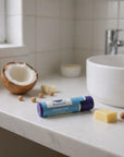 Tube of unscented lip balm on bathroom countertop with coconut and shea butter ingredients nearby