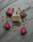 Bar of soap with pink flowers and yellow petals on a marble surface