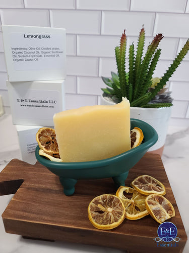 Lemongrass soap bar on a wooden tray with dried lemons, plant in background.