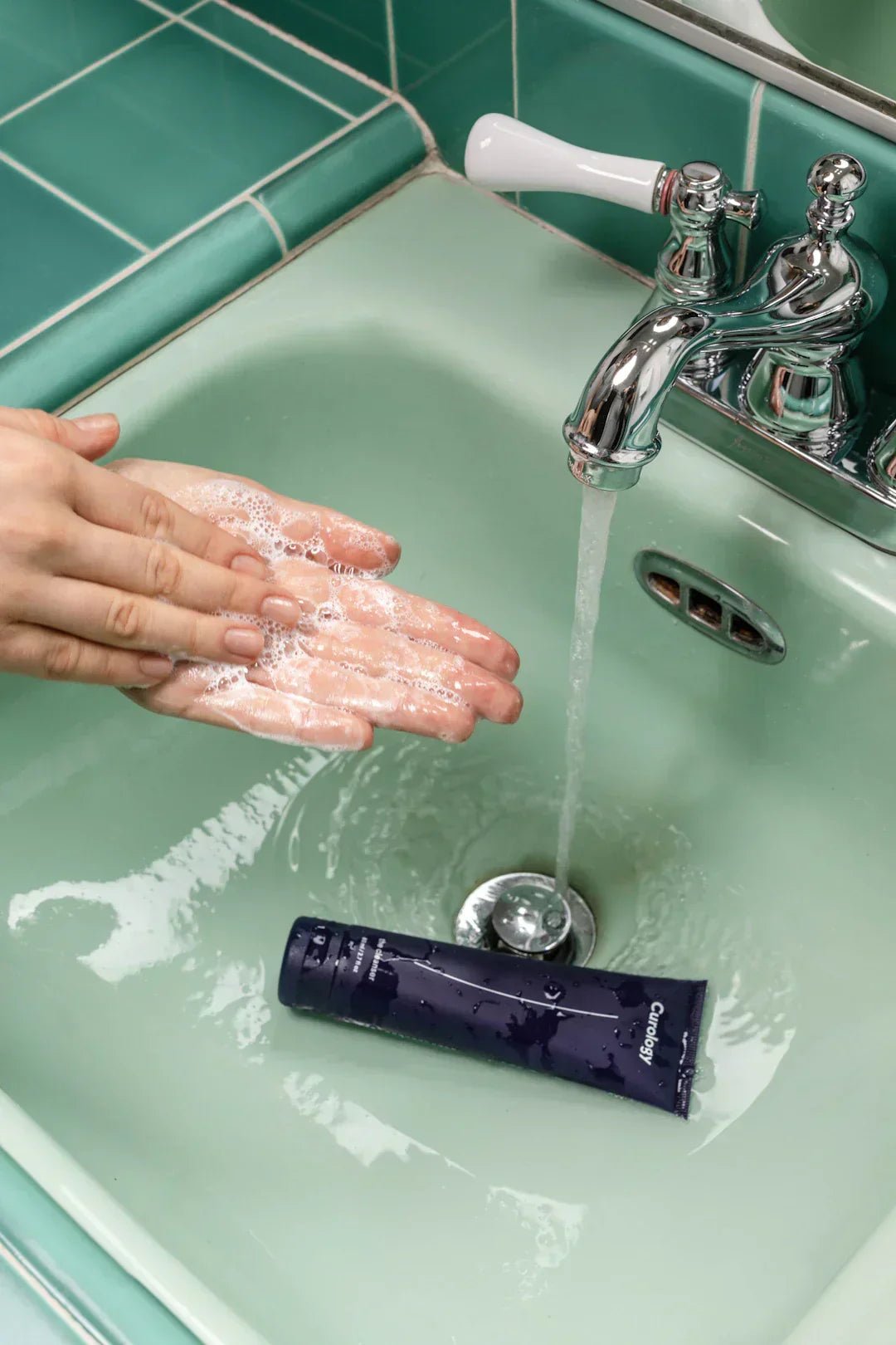 Hands washing with soap under running water in a green sink.