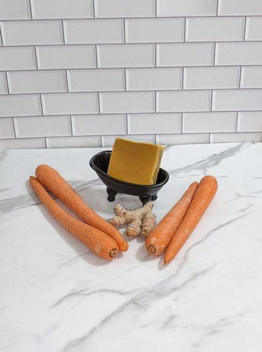 Carrot and turmeric bar soap with fresh vegetables on marble surface.