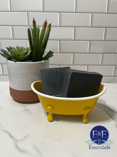 Charcoal soap bars in a decorative yellow dish with succulents in the background.