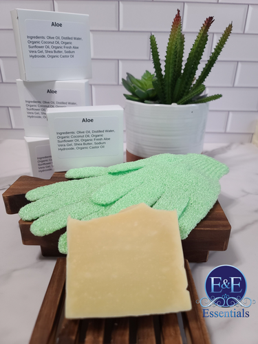 Aloe and shea butter soap with green exfoliating gloves and aloe plant on wooden tray.