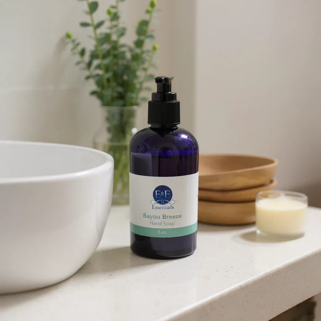 Bayou Breeze Hand Soap in a blue pump bottle on a bathroom counter with white sink and wooden bowls in the background
