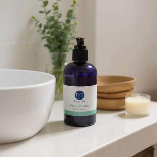 Bayou Breeze Hand Soap in a blue pump bottle on a bathroom counter with white sink and wooden bowls in the background
