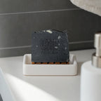 Activated charcoal soap bar on a white soap dish with a dark tiled background, designed for deep cleansing and detoxifying skin.