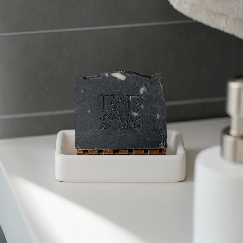 Activated charcoal soap bar on a white soap dish with a dark tiled background, designed for deep cleansing and detoxifying skin.