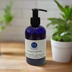 Blue bottle of E&E Essentials Lemongrass Hand Soap on a wooden surface with plants in the background