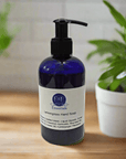 Blue bottle of E&E Essentials Lemongrass Hand Soap on a wooden surface with plants in the background