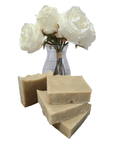 Three bars of soap stacked with a clear vase containing white roses on a white background
