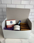 White gift box with lid containing items for display, against a tiled background.