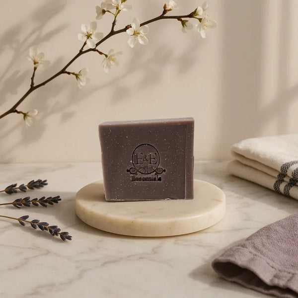Lavender bar soap on marble dish with lavender sprigs and folded towels, natural calming skincare product.