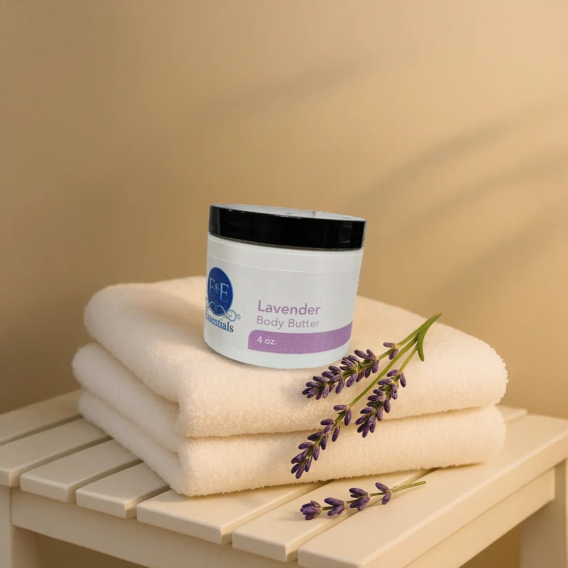 Jar of Lavender Whipped Body Butter on stacked beige towels with fresh lavender sprigs on a wooden surface