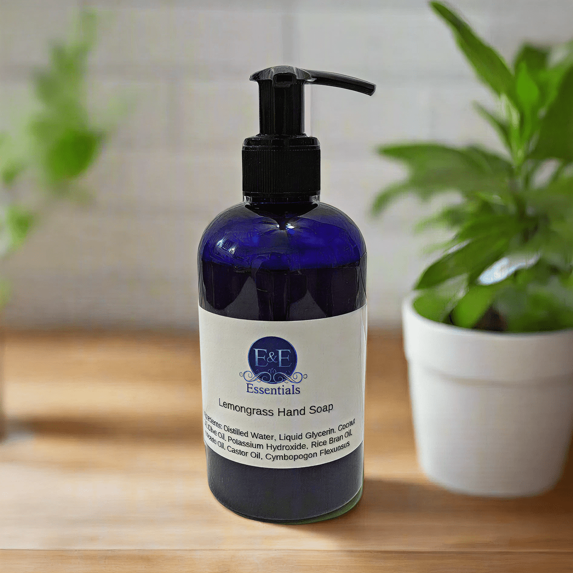 Lemongrass Hand Soap blue bottle on wooden counter with green plants, E &amp; E Essentials label visible