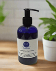 Lemongrass Hand Soap blue bottle on wooden counter with green plants, E & E Essentials label visible