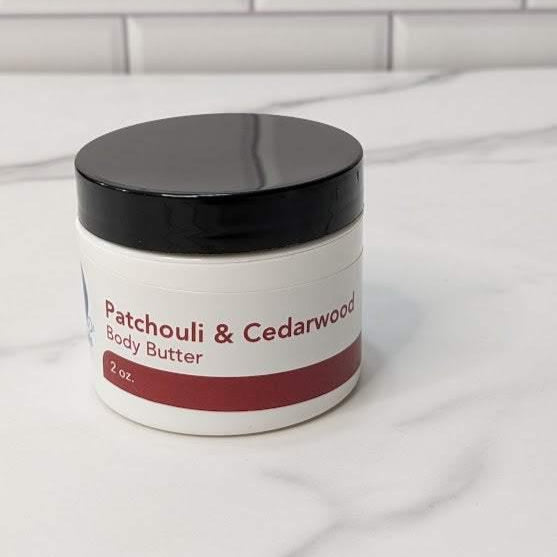 Patchouli & Cedarwood Body Butter jar on marble surface, offering luxurious hydration and warm, earthy aroma.