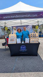 Two people standing behind a table with E&F Essentials products under a branded tent.