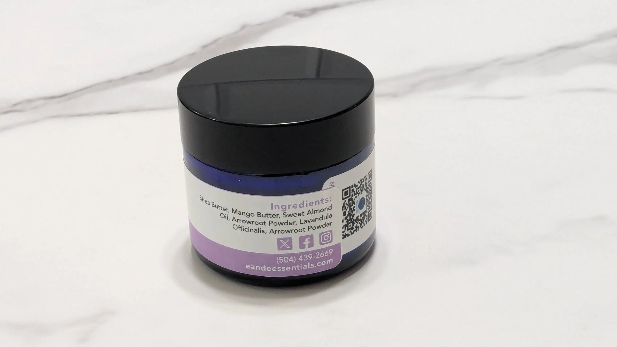 A small blue glass jar of pure butter with a white and purple label, placed on a white marble surface.