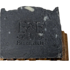 Activated charcoal soap bar on wooden soap holder showing brand imprint.