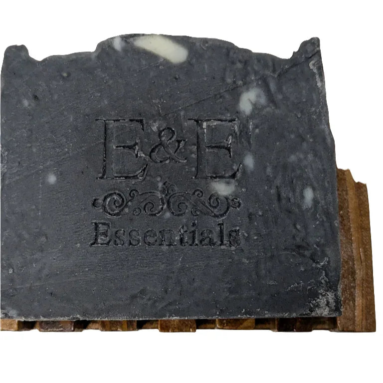 Activated charcoal soap bar on wooden soap holder showing brand imprint.