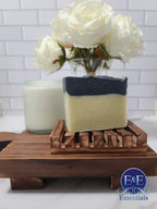 Charcoal and sea clay bar soap on wooden dish with candle and roses in background