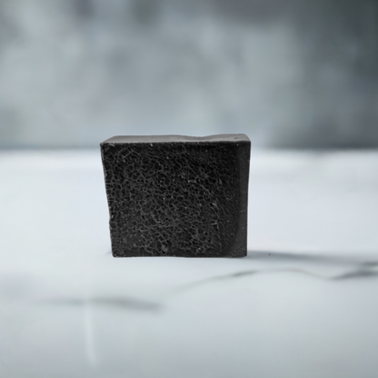 Charcoal bar soap resting on a white countertop, emphasizing its color contrast