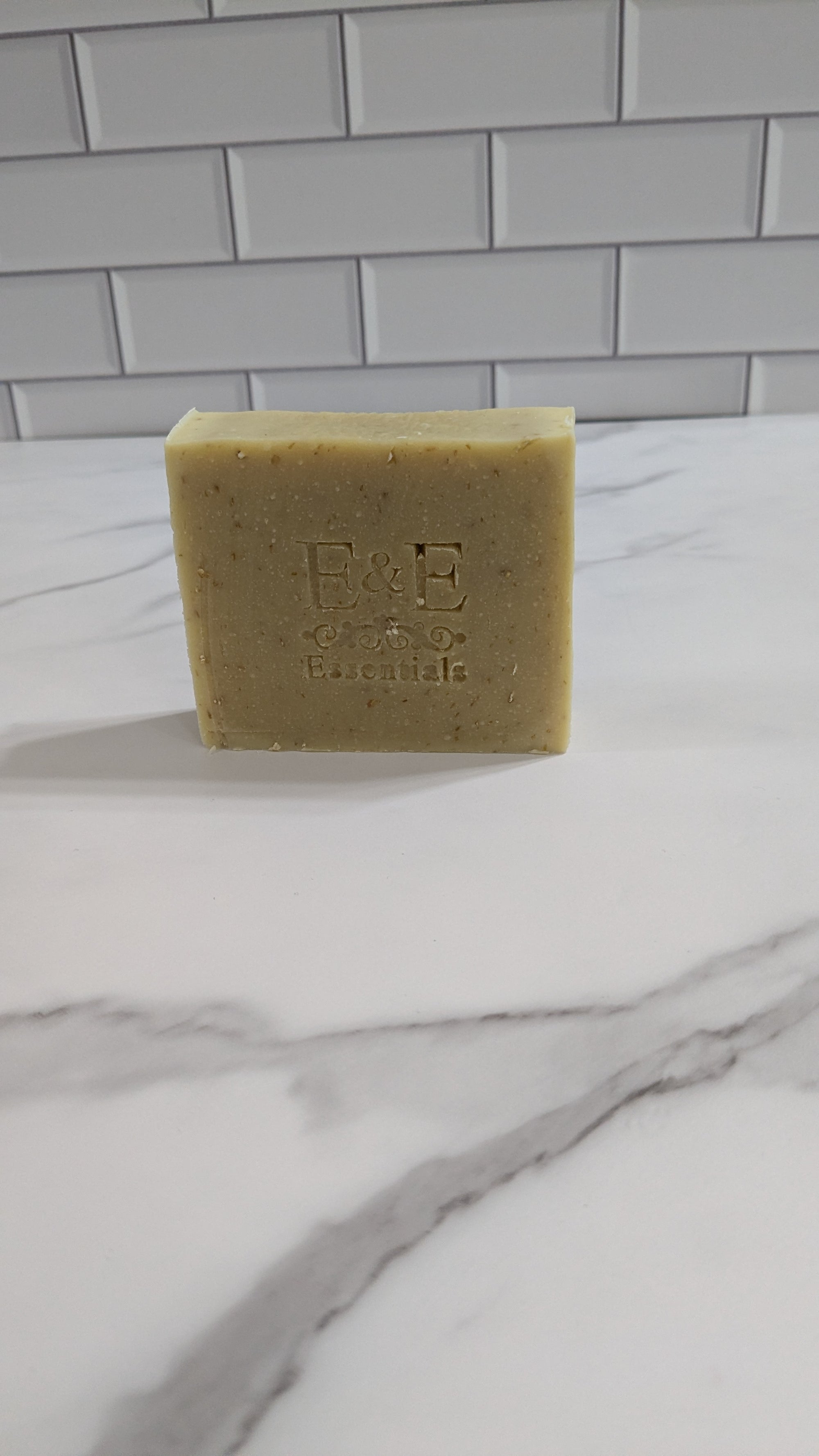 Bar of soap with 'E&E' branding on a marble surface against a tiled wall background