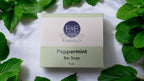 Peppermint Bar Soap packaging surrounded by fresh mint leaves.