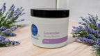 Lavender Whipped Body Butter jar amidst fresh lavender sprigs on a wooden surface.