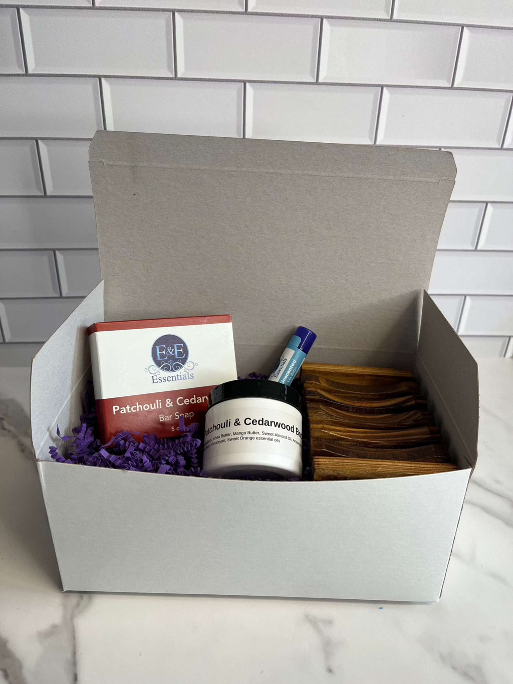 White gift box with lid containing items for display, against a tiled background.