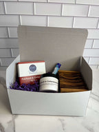 White gift box with lid containing items for display, against a tiled background.