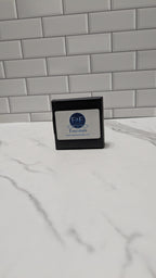 Small black box with a label on a white surface against a gray tiled wall.