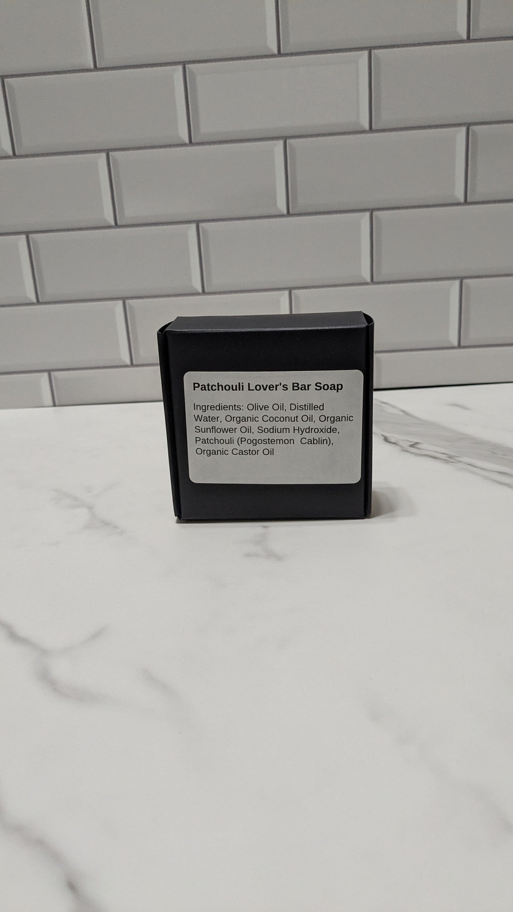 Bar of soap in a black container with a label on a marble surface.