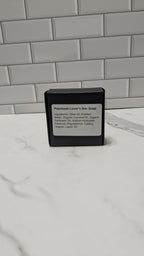Bar of soap in a black container with a label on a marble surface.